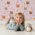 Lovely child standing in front of Whimsy Tots Woodland Tribe Hearts Wallpaper in Blush Lilac Pink with bear, fox, rabbit, feather, arrow, heart in design.
