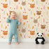 Lovely child standing in front of Whimsy Tots Woodland Tribe Hearts Wallpaper in Vanilla Cream with bear, fox, rabbit, feather, arrow, heart in design.