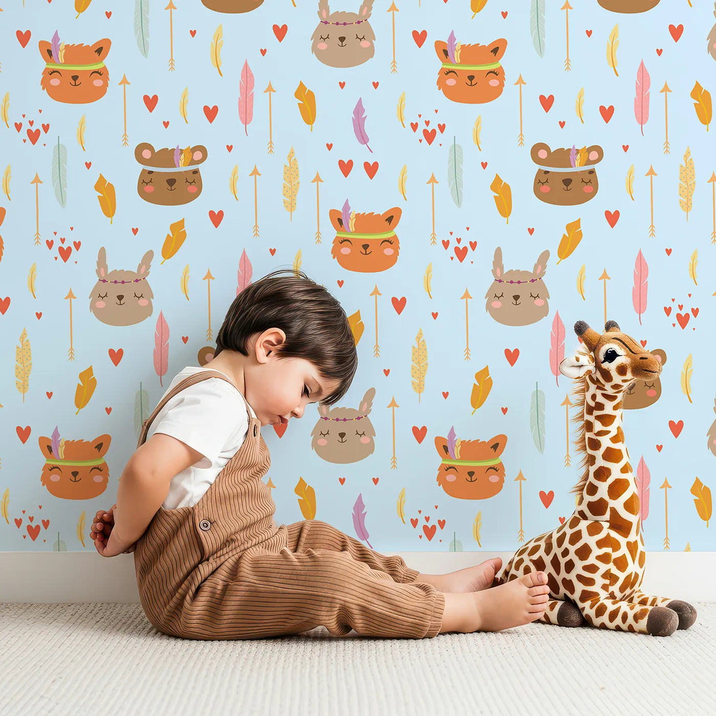 Lovely child standing in front of Whimsy Tots Woodland Tribe Hearts Wallpaper in Sky Blue with bear, fox, rabbit, feather, arrow, heart in design.