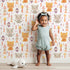 Lovely child standing in front of Whimsy Tots Mindful Kitten Heart Wallpaper in Vanilla Cream with cat, heart, triangle, dot, diamond in design.