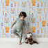 Lovely child standing in front of Whimsy Tots Mindful Kitten Heart Wallpaper in Sky Blue with cat, heart, triangle, dot, diamond in design.