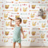 Lovely child standing in front of Whimsy Tots Tribal Bunny Parade Wallpaper in Vanilla Cream with rabbit, arrow, feather, diamond in design.