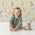 Lovely child standing in front of Whimsy Tots Feather Arrow Confetti Wallpaper in Mint Whisper Green with arrow, feather, triangle, dot in design.