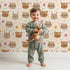 Lovely child standing in front of Whimsy Tots Feather Crown Critters Wallpaper in Beige with bear, rabbit, crown, feather, arrow, dot in design.