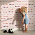 Lovely child standing in front of Whimsy Tots Boho Arrow Trail Wallpaper in Blush Pink with arrow, diamond in design.