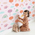 Lovely child standing in front of Whimsy Tots Birdie Rainbow Float Parade Wallpaper in Blush Dream Pink with bird, balloon, rainbow, heart, cloud in design.