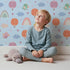 Lovely child standing in front of Whimsy Tots Birdie Rainbow Float Parade Wallpaper in Sky Breeze with bird, balloon, rainbow, heart, cloud in design.