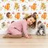 Lovely child standing in front of Whimsy Tots Cuddle Buddies Parade Wallpaper in White with fox, bird, badger, cat, heart, flower in design.