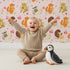 Lovely child standing in front of Whimsy Tots Cuddle Buddies Parade Wallpaper in Blush Pink with fox, bird, badger, cat, heart, flower in design.