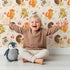 Lovely child standing in front of Whimsy Tots Cuddle Buddies Parade Wallpaper in Cream with fox, bird, badger, cat, heart, flower in design.