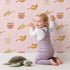Lovely child standing in front of Whimsy Tots Feathered Friends and Fuzzy Faces Parade Wallpaper in Blush with cat, fox, bird, feather, star in design.