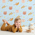 Lovely child standing in front of Whimsy Tots Feathered Friends and Fuzzy Faces Parade Wallpaper in Blue with cat, fox, bird, feather, star in design.