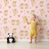 Lovely child standing in front of Whimsy Tots Heartful Bunny Parade Wallpaper in Blush Pink with rabbit, heart in design.