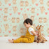 Lovely child standing in front of Whimsy Tots Heartful Bunny Parade Wallpaper in Mint Green with rabbit, heart in design.