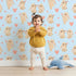 Lovely child standing in front of Whimsy Tots Heartful Bunny Parade Wallpaper in Sky Blue with rabbit, heart in design.