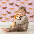 Lovely child standing in front of Whimsy Tots Dreamy Pony Meadow Wallpaper in Blush Pink with horse, flower, leaf, dot in design.