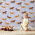 Lovely child standing in front of Whimsy Tots Dreamy Pony Meadow Wallpaper in Lavender Sky with horse, flower, leaf, dot in design.