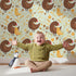 Lovely child standing in front of Whimsy Tots Hen and Chick Meadow Wallpaper in Soft Sage Green with chicken, chick, flower, leaf in design.