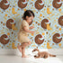 Lovely child standing in front of Whimsy Tots Hen and Chick Meadow Wallpaper in Sky Blue with chicken, chick, flower, leaf in design.