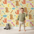 Lovely child standing in front of Whimsy Tots Arrow Pup and Foxy Night Parade Wallpaper in Dandelion with dog, fox, moon, arrow, star, cloud in design.
