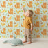 Lovely child standing in front of Whimsy Tots Fox and Finch Woodland Waltz Wallpaper in Mint Green with fox, bird, acorn, leaf, flower in design.