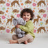 Lovely child standing in front of Whimsy Tots Blossom Meadow Deer Wallpaper in White with deer, flower, butterfly, heart in design.