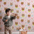 Lovely child standing in front of Whimsy Tots Heart Bloom Critters Wallpaper in Blush Pink with bear, rabbit, owl, heart, flower, cloud in design.