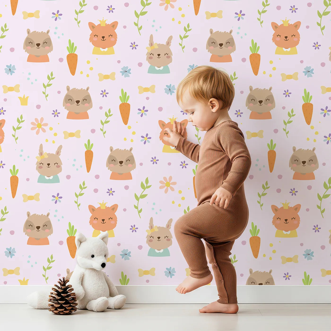 Lovely child standing in front of Whimsy Tots Meadow Crown Friends Wallpaper in Blush Pink with fox, rabbit, bear, flower, carrot, crown, bow in design.