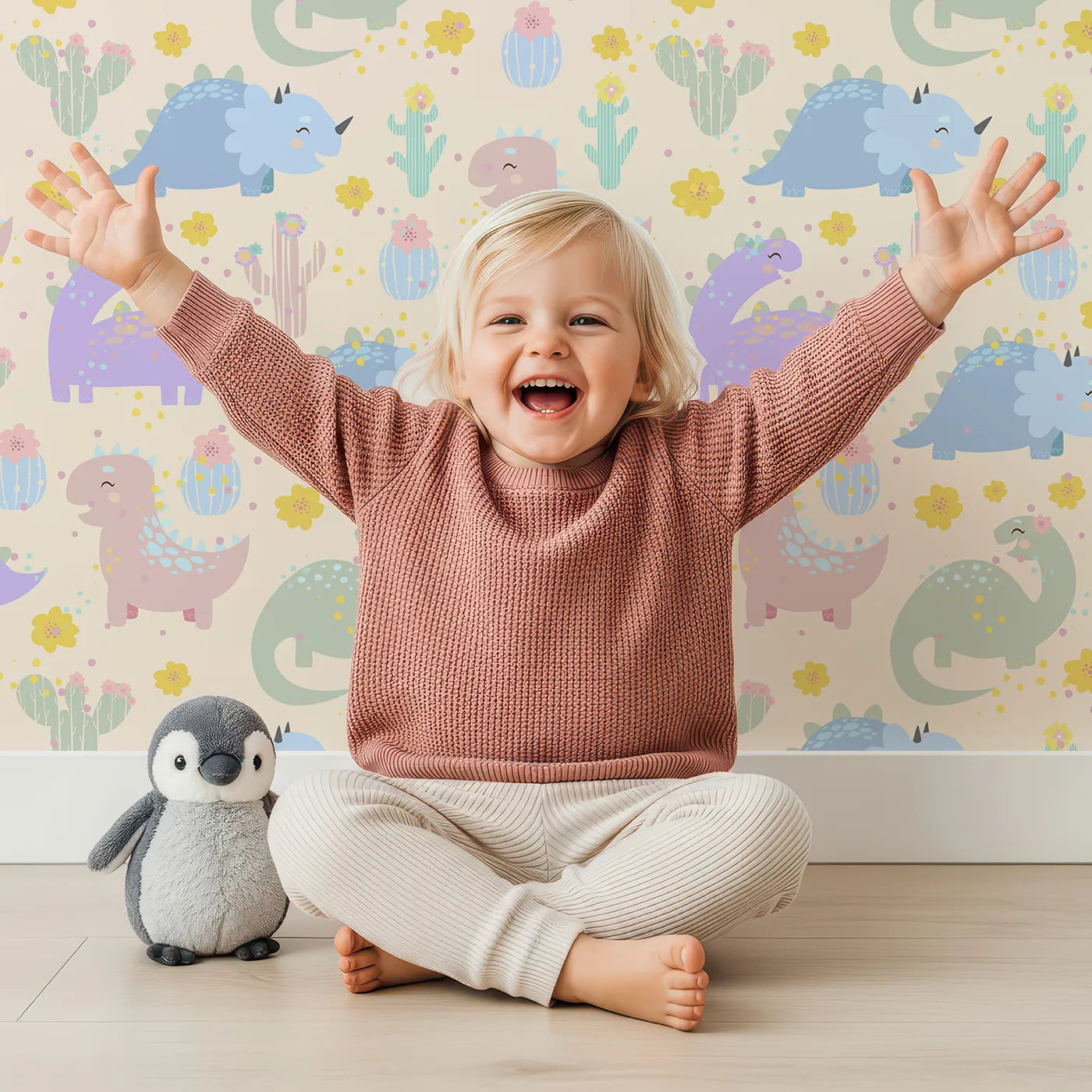Lovely child standing in front of Whimsy Tots Cactus Dino Parade Wallpaper in Cream with dinosaur, cactus, flower in design.