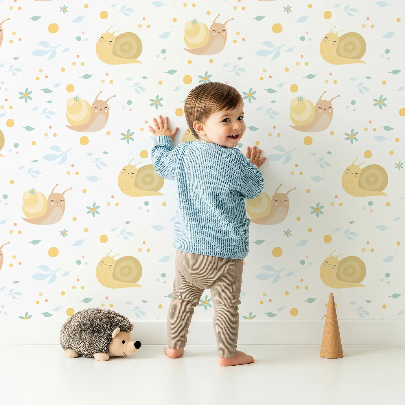Lovely child standing in front of Whimsy Tots Snail Meadow Cuddle Parade Wallpaper in White with snail, flower, leaf in design.