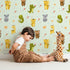 Lovely child standing in front of Whimsy Tots Wild Heart Animal Parade Wallpaper in Mint Green with giraffe, koala, leopard, monkey, tiger, crocodile, heart, arrow, star in design.