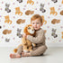 Lovely child standing in front of Whimsy Tots Blossom Fox Nap Parade Wallpaper in White with fox, flower, star in design.