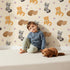 Lovely child standing in front of Whimsy Tots Blossom Fox Nap Parade Wallpaper in Cream with fox, flower, star in design.