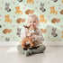 Lovely child standing in front of Whimsy Tots Blossom Fox Nap Parade Wallpaper in Mint Green with fox, flower, star in design.
