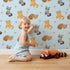 Lovely child standing in front of Whimsy Tots Blossom Fox Nap Parade Wallpaper in Sky Blue with fox, flower, star in design.
