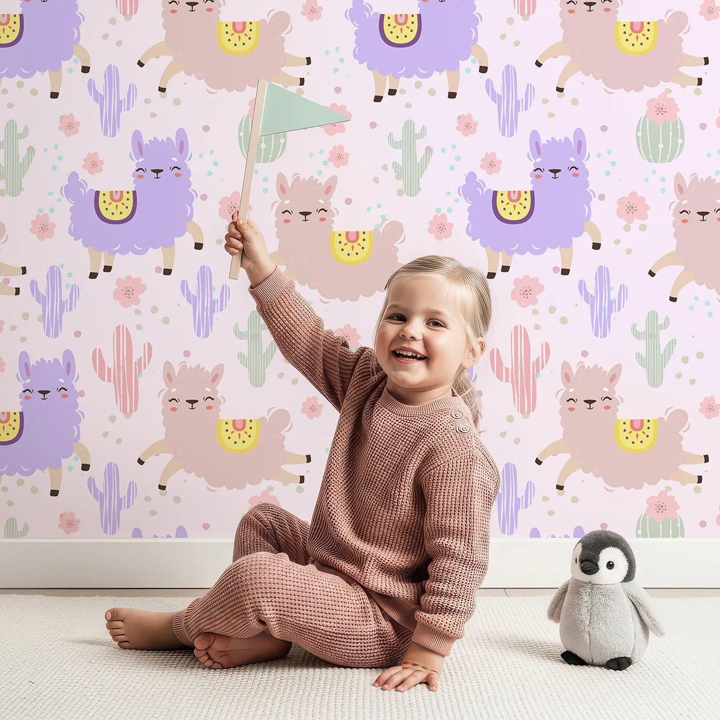 Lovely child standing in front of Whimsy Tots Bouncing Llama Fiesta Wallpaper in Pink Blush with llama, cactus, flower, confetti in design.