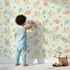 Lovely child standing in front of Whimsy Tots Sunbeam Wildflower Parade Wallpaper in Mint Green with flower, wildflower, leaf, bouquet in design.