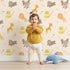 Lovely child standing in front of Whimsy Tots Safari Buddies Parade Wallpaper in Blush Pink with lion, giraffe, elephant, hippo, tiger, arrow in design.