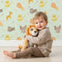 Lovely child standing in front of Whimsy Tots Safari Buddies Parade Wallpaper in Mint Green with lion, giraffe, elephant, hippo, tiger, arrow in design.