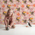 Lovely child standing in front of Whimsy Tots Tropical Toucan Friends Wallpaper in Pink with toucan, flower, leaf, hibiscus in design.
