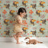 Lovely child standing in front of Whimsy Tots Tropical Toucan Friends Wallpaper in Mint Green with toucan, flower, leaf, hibiscus in design.