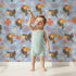 Lovely child standing in front of Whimsy Tots Tropical Toucan Friends Wallpaper in Blue with toucan, flower, leaf, hibiscus in design.