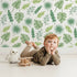 Lovely child standing in front of Whimsy Tots Tropical Leaf Mix Wallpaper in White with leaf, monstera, palm, jungle in design.