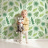 Lovely child standing in front of Whimsy Tots Tropical Leaf Mix Wallpaper in Mint Green with leaf, monstera, palm, jungle in design.