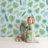 Lovely child standing in front of Whimsy Tots Tropical Leaf Mix Wallpaper in Blue with leaf, monstera, palm, jungle in design.