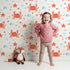 Lovely child standing in front of Whimsy Tots Crabby Coral Dance Wallpaper in White with crab, starfish, shell, coral, sand in design.