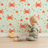 Lovely child standing in front of Whimsy Tots Crabby Coral Dance Wallpaper in Mint Green with crab, starfish, shell, coral, sand in design.