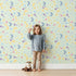 Lovely child standing in front of Whimsy Tots Starlit Wishes Wallpaper in Mint Green with moon, star, constellation, shooting star, galaxy in design.