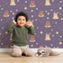 Lovely child standing in front of Whimsy Tots Starry Snuggle Pals Wallpaper in Plum with bear, rabbit, star, heart, constellation in design.