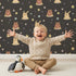 Lovely child standing in front of Whimsy Tots Starry Snuggle Pals Wallpaper in Charcoal Gray with bear, rabbit, star, heart, constellation in design.